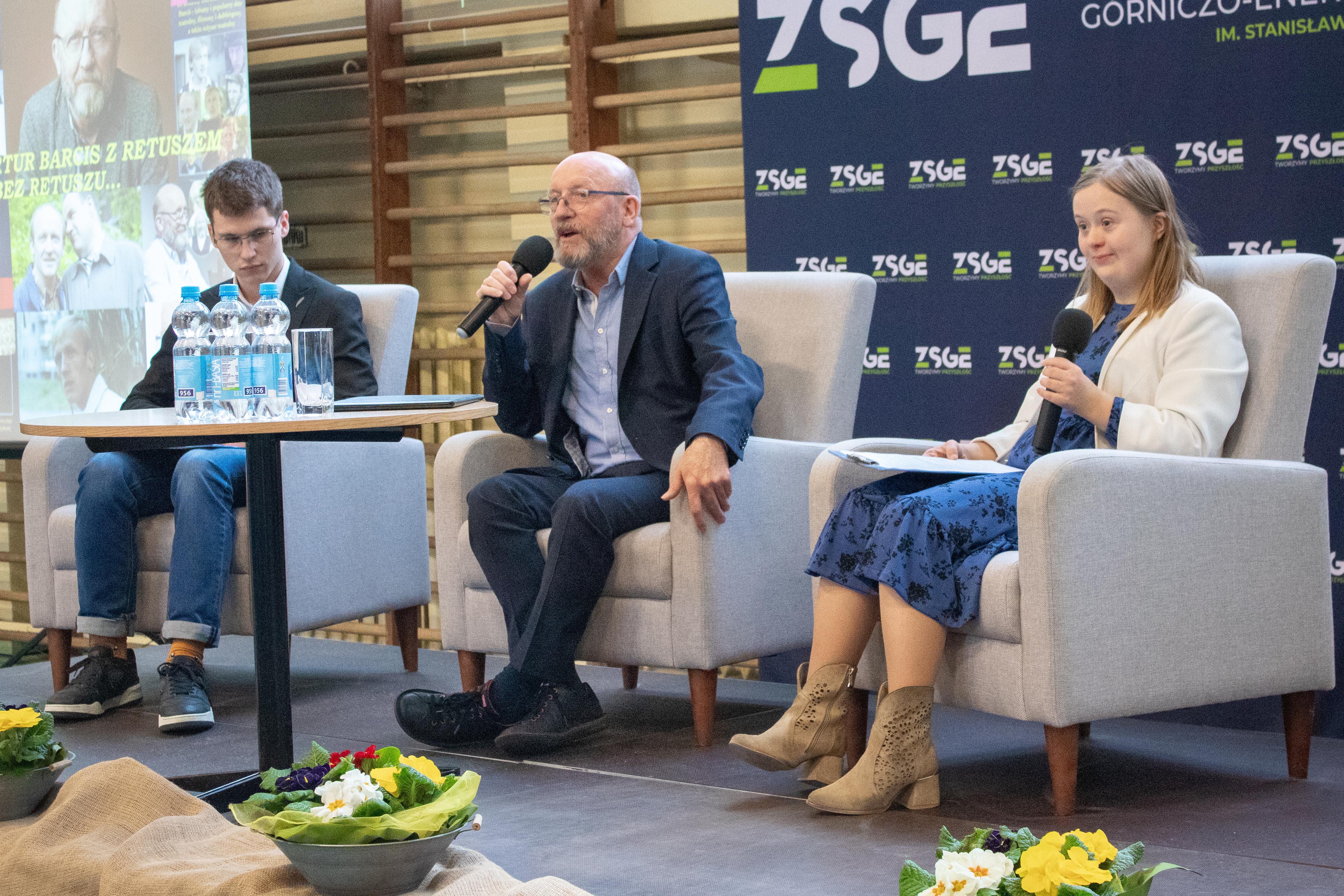 na fotelach siedzą trzy osoby, w środku mężczyzna z mikrofonem, z jednej strony chłopak z drugiej dziewczyna